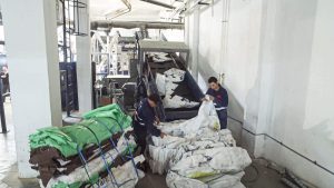 Mitarbeitende befördern mittels Fließband Plastiksäcke und Folien in den Schredder WLK1500