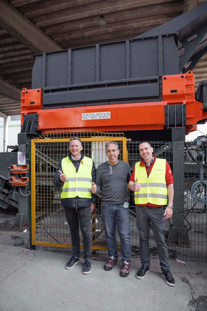 three weima employees with yellow warning vests in front of an orange weima shredder