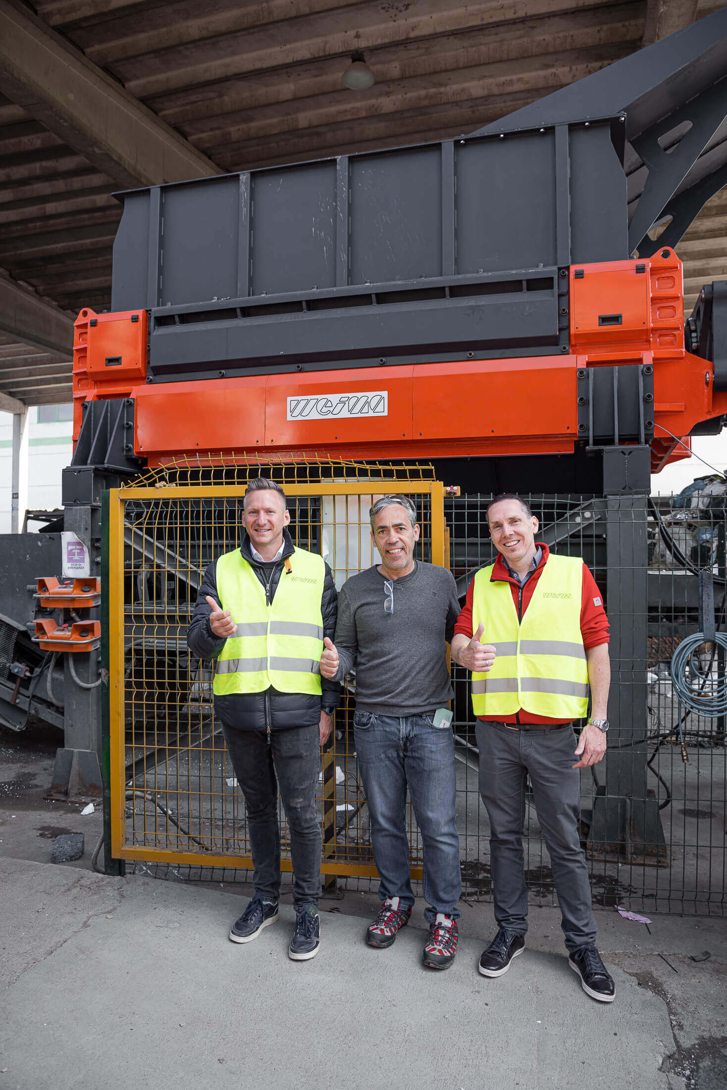 three weima employees with yellow warning vests in front of an orange weima shredder