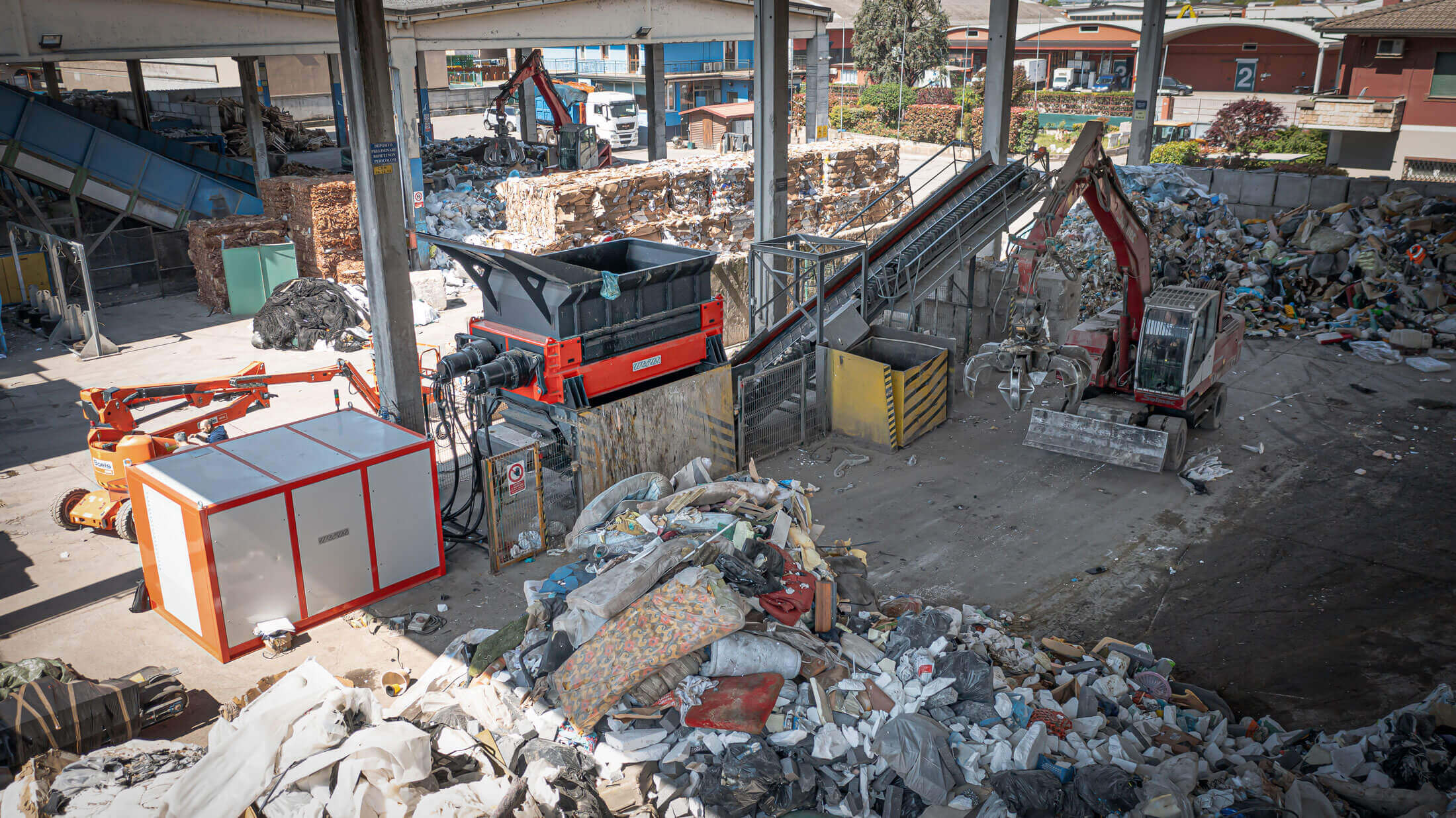 orange weima shredder with hydraulic drive and piles of household waste
