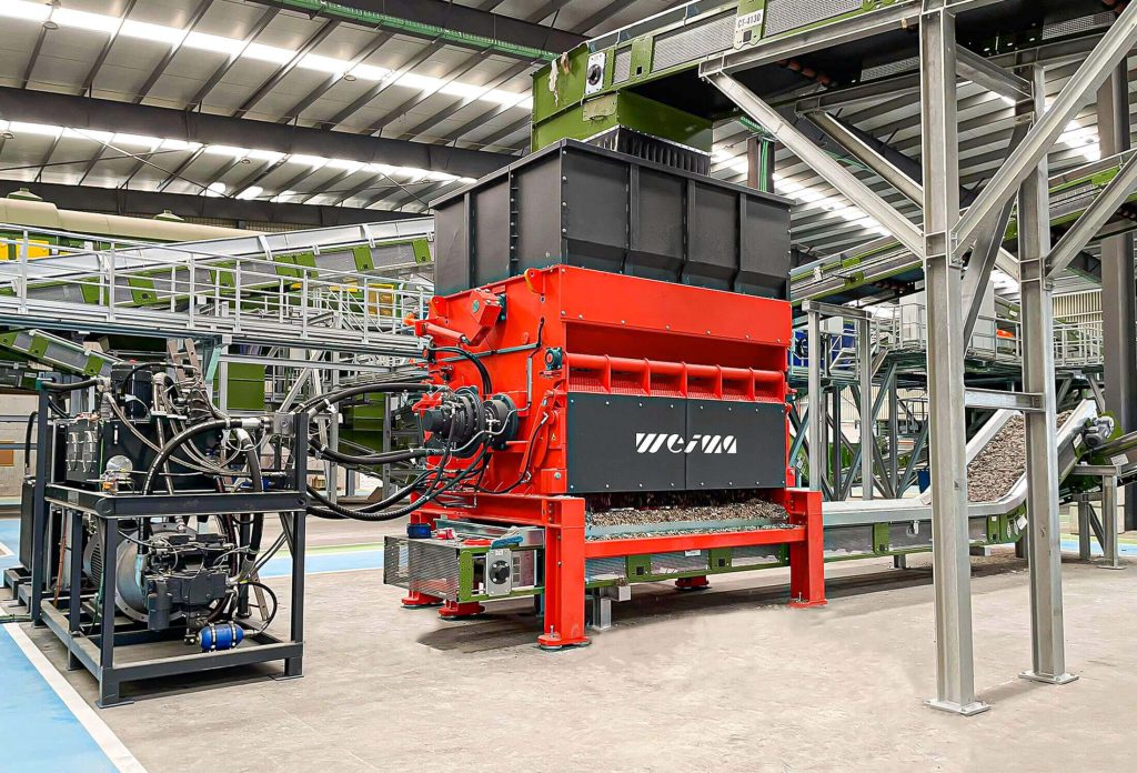 orange weima shredder next to conveyor belt inside hall for municipal waste treatment (MSW)