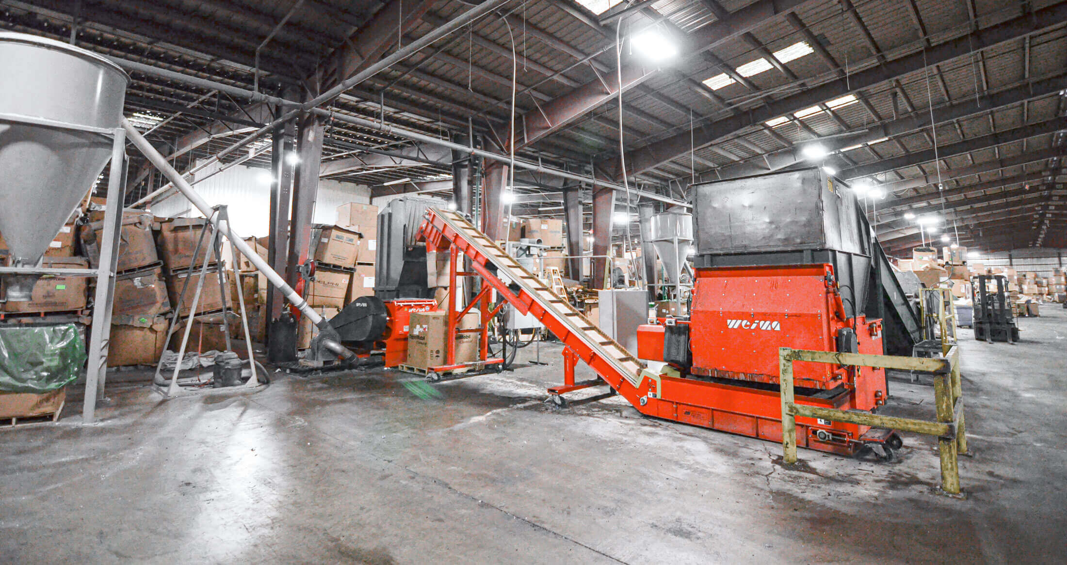 WEIMA shredder with conveyor belt in a recycling hall for two-stage plastic shredding.