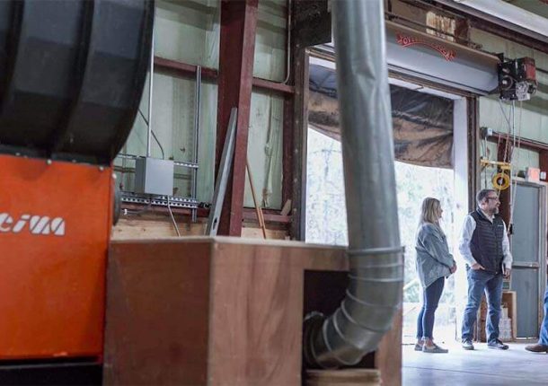 Three people are standing and speaking with each other in a warehouse next to an orange WEIMA shredder.