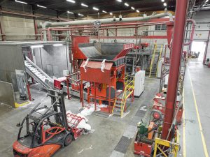 View from above into an industrial hall, in the centre is an orange-red shredder, in the foreground you can see a forklift truck