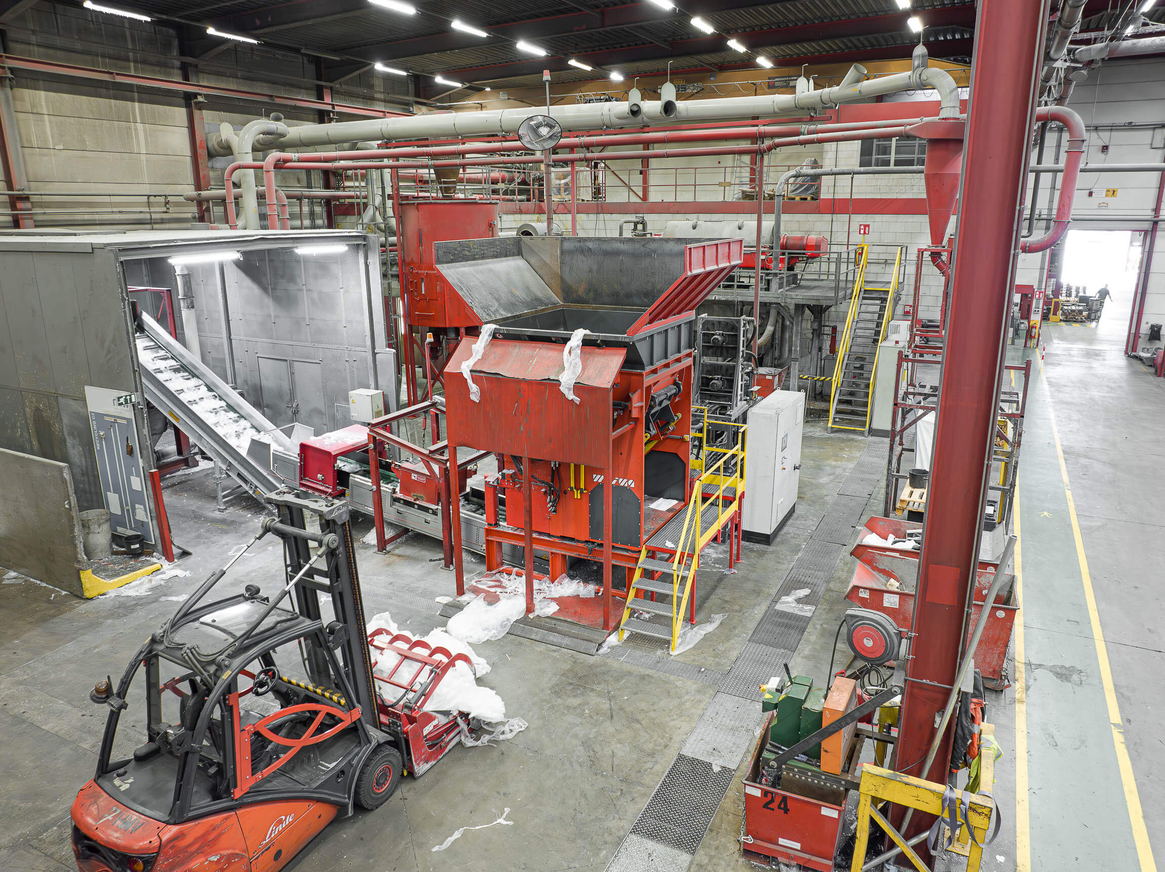 View from above into an industrial hall, in the centre is an orange-red shredder, in the foreground you can see a forklift truck