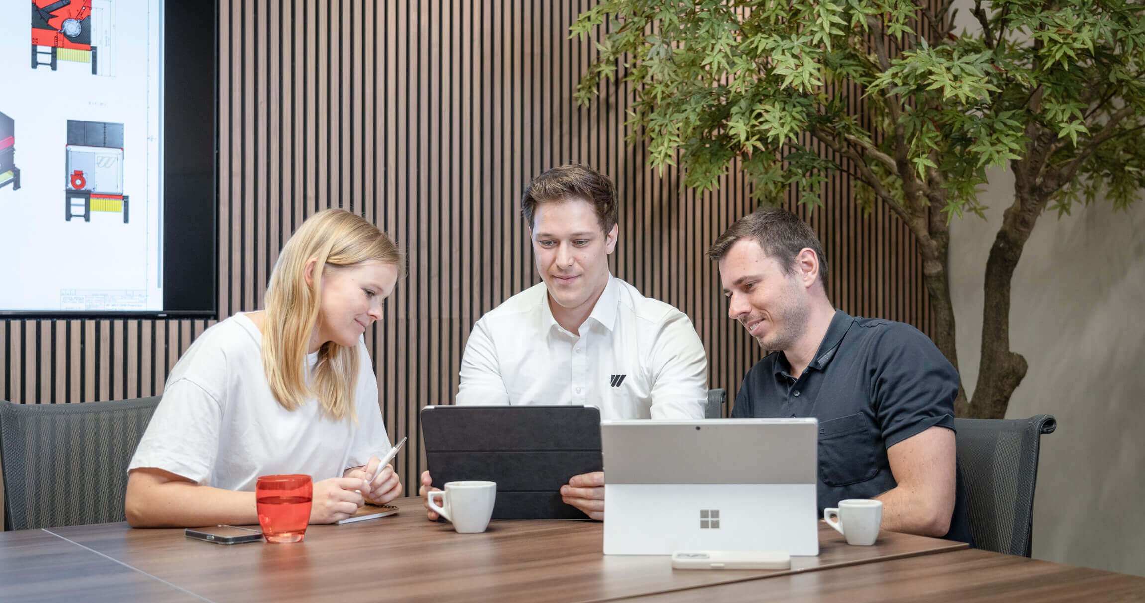 a woman and two men working together in front of computers in a conference room
