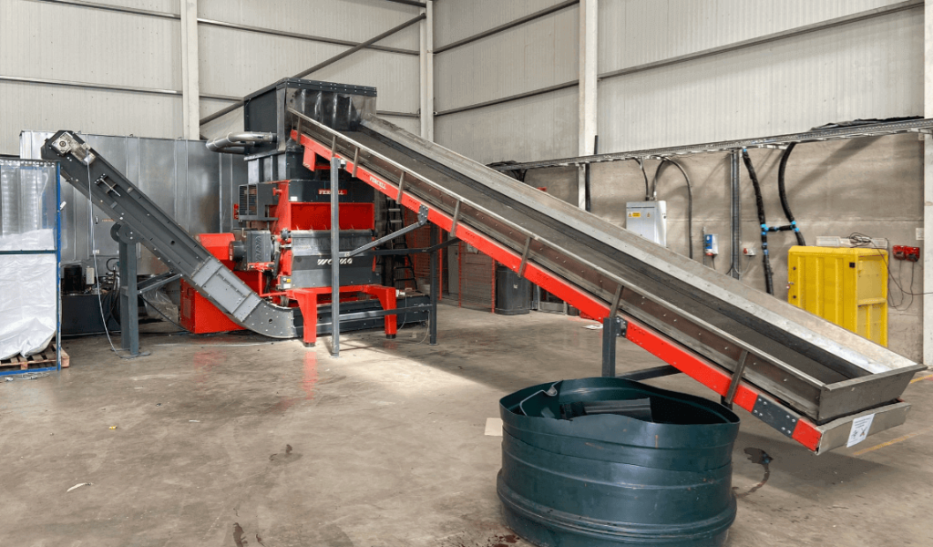 An orange shredder with a conveyor belt in an industrial hall