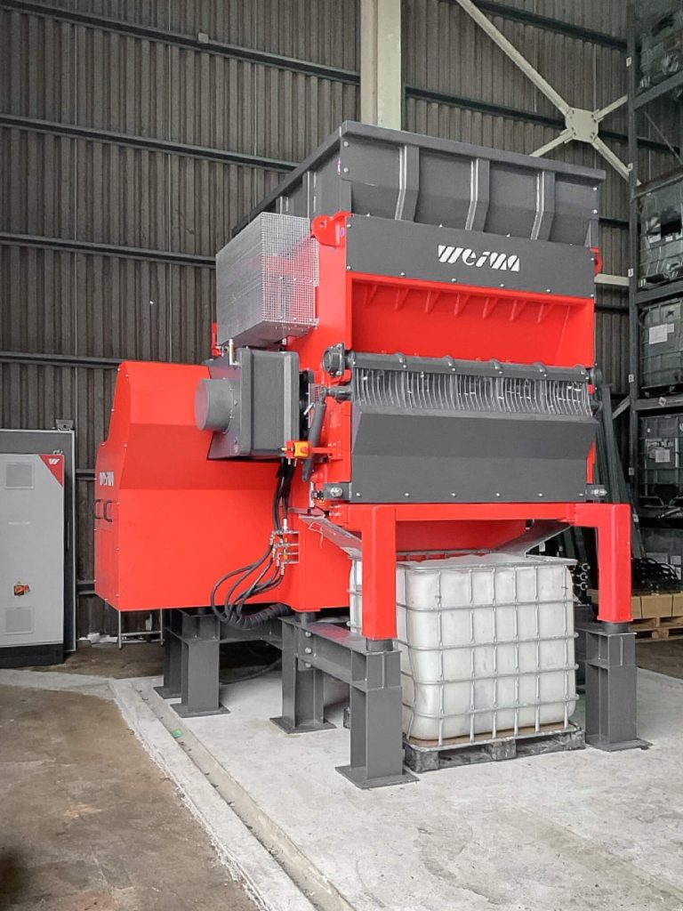 An orange shredder in a warehouse with an IBC container under the machine.