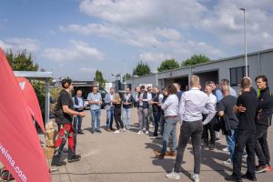 A group stands in a semicircle in front of a company site