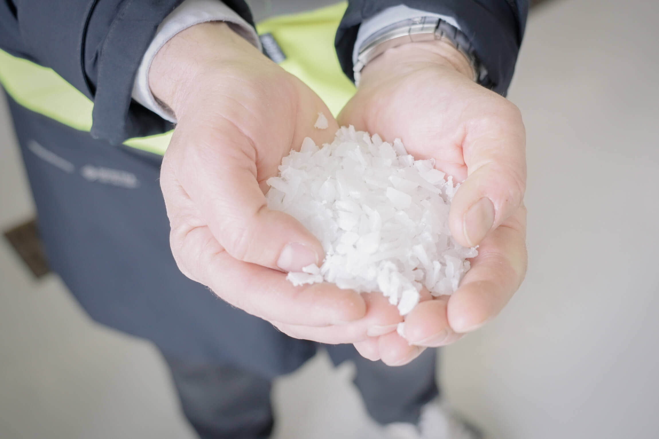 a person in a black and yellow jacket holds IBC recyclate in his hand after the recycling process