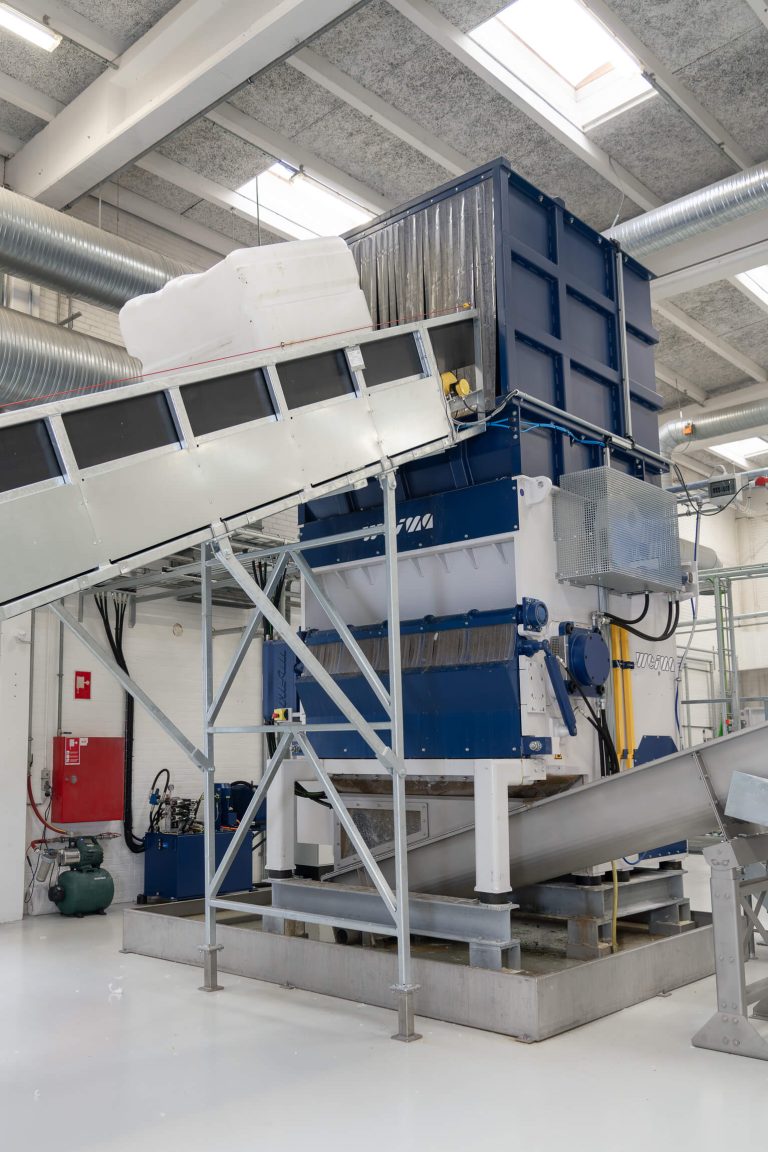 An IBC container is transported via a conveyor belt into a WEIMA shredder.