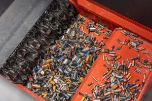 A large number of used batteries in an orange shredder during shredding