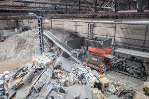 Top view of a WEIMA shredder with conveyor belt. Material for shredding is in the area in front of the shredder, the shredded material comes after the conveyor belt