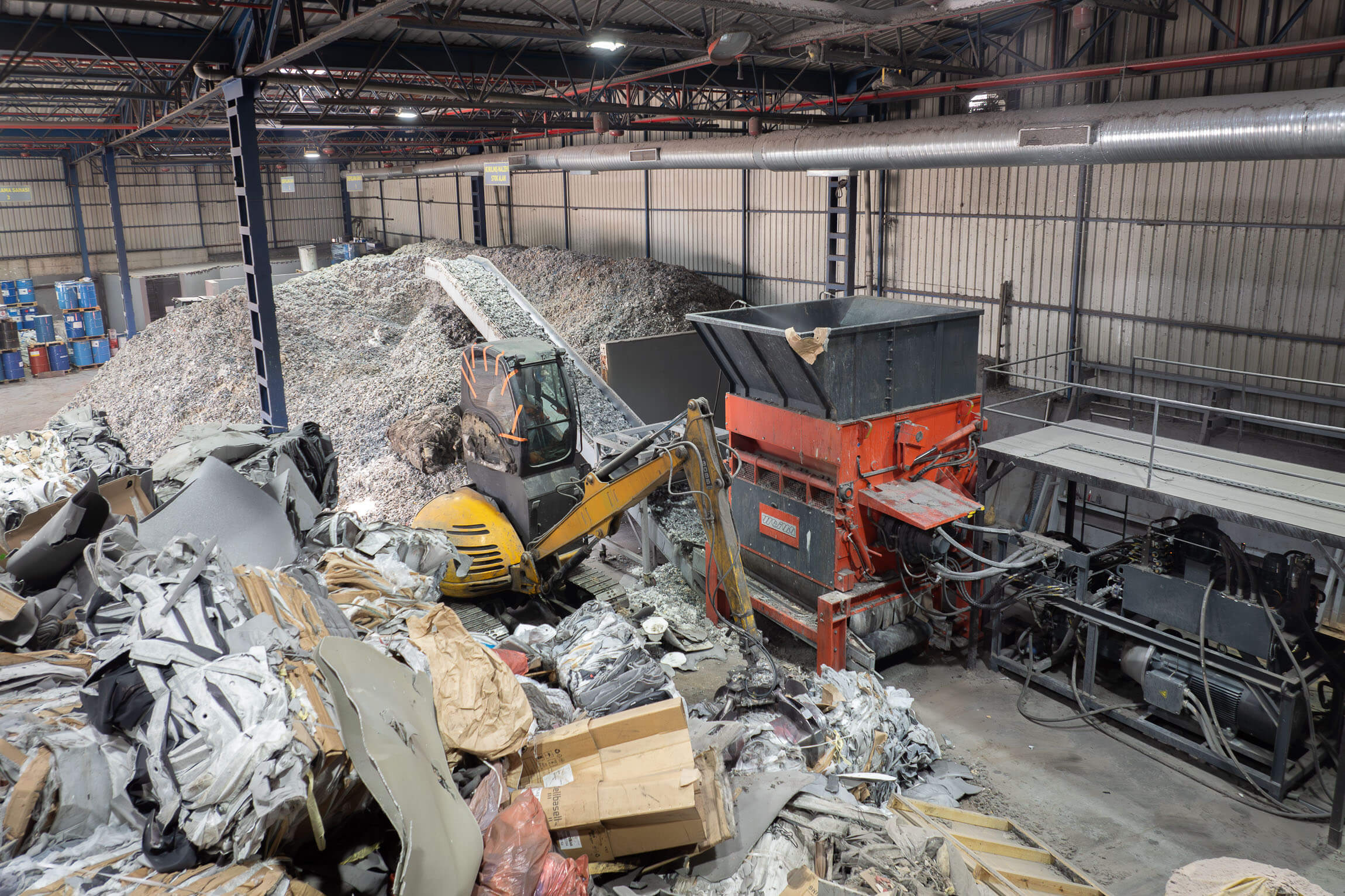 Top view of a WEIMA shredder with conveyor belt. Material for shredding lies in the area in front of the shredder and is transported into the shredder by an excavator; the shredded material comes after the conveyor belt