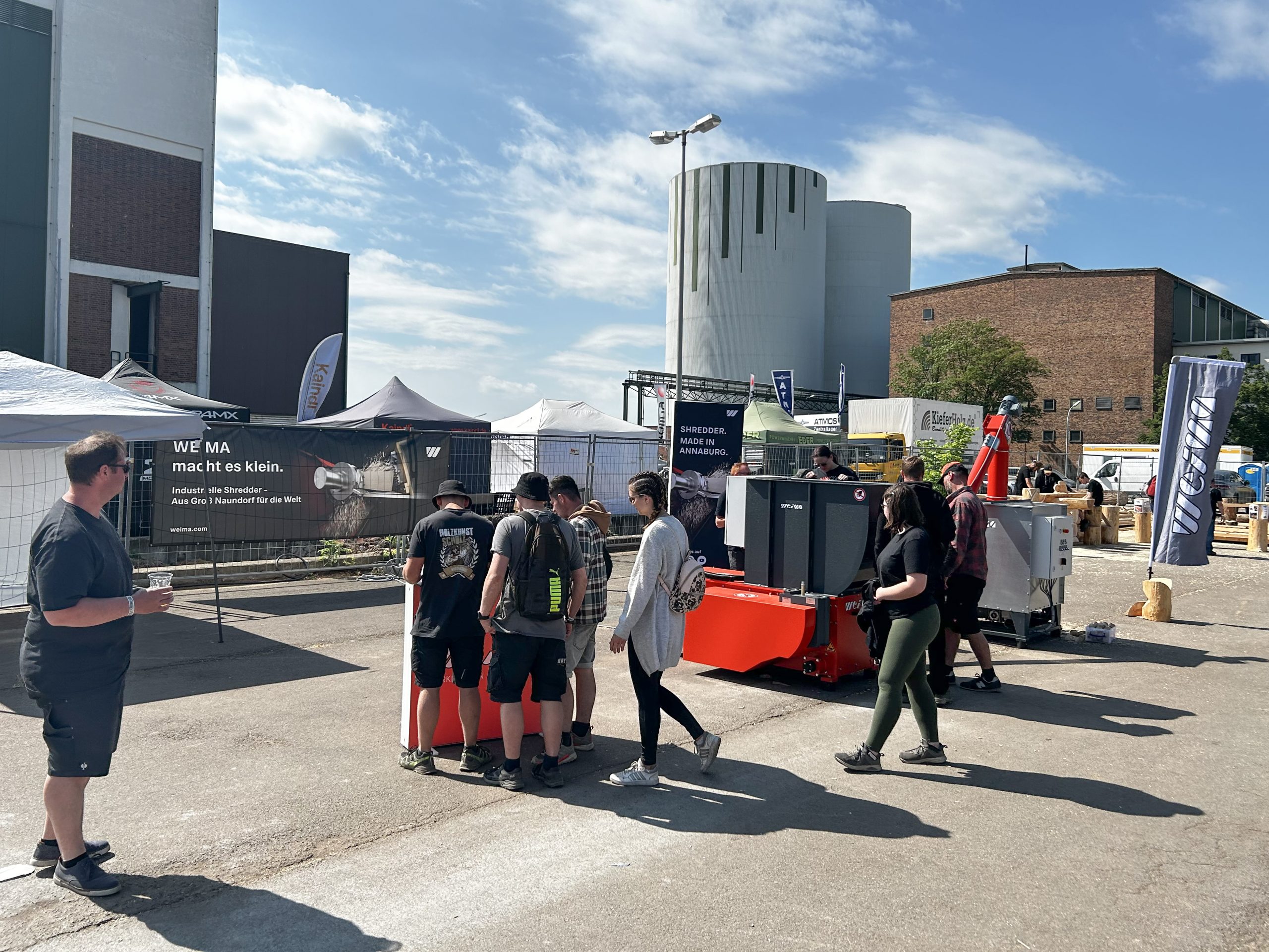Several people in front of an orange shredder on an industrial site during a festival