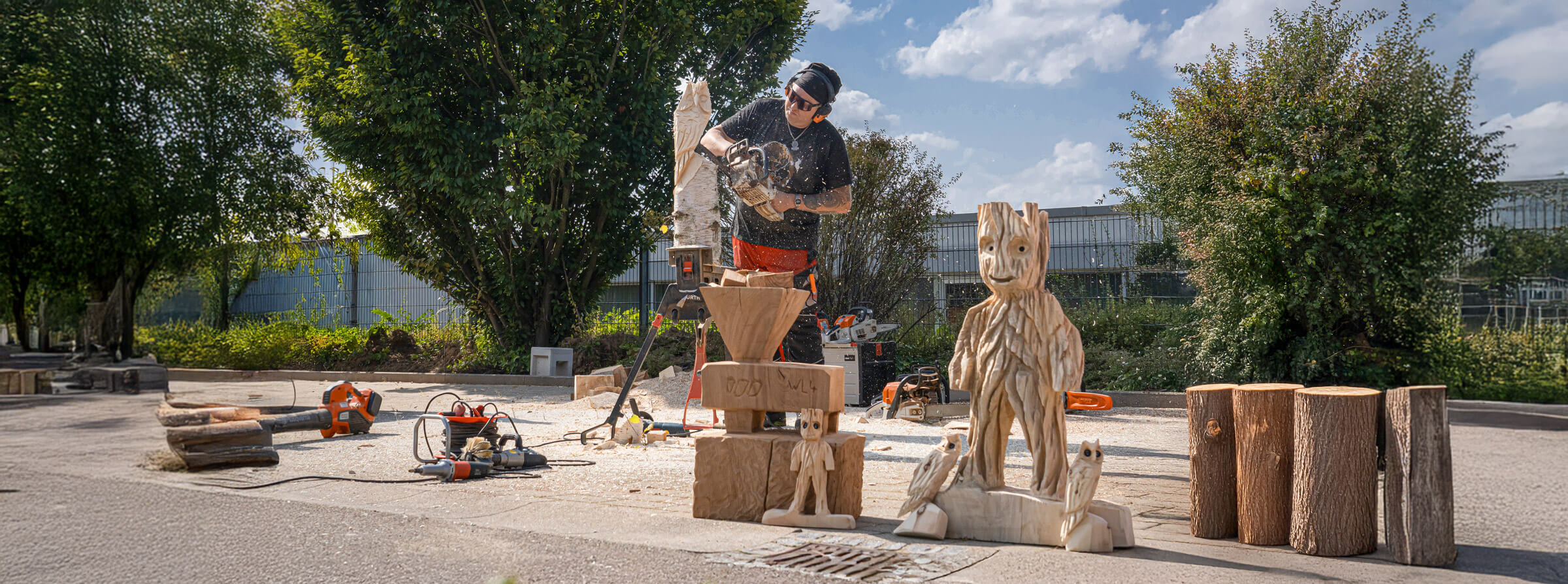 A man saws an owl out of a block of wood while some finished figures are already standing in the foreground