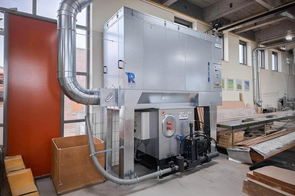 Silver briquette press from WEIMA under a large gray extraction system in a production hall