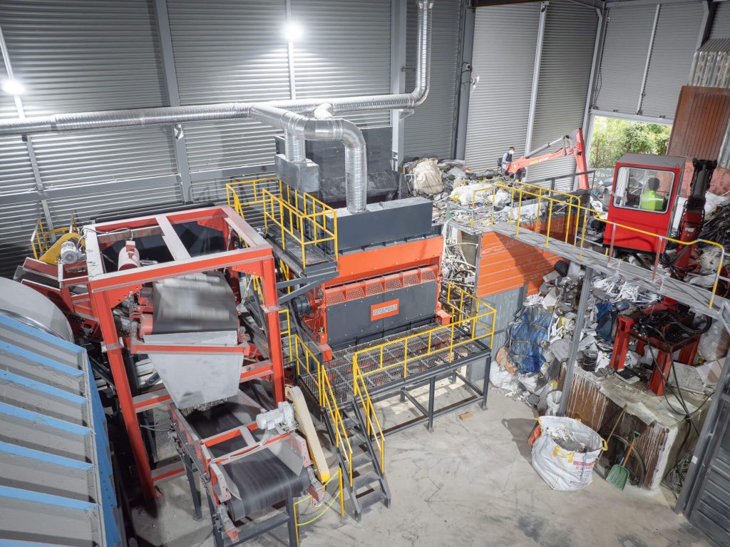 Aerial view of an orange shredder installed in a warehouse between a crane for filling and a magnetic belt