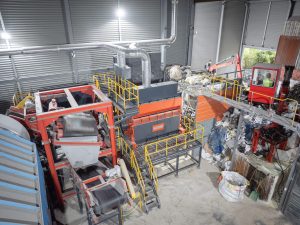 Aerial view of an orange shredder installed in a warehouse between a crane for filling and a magnetic belt