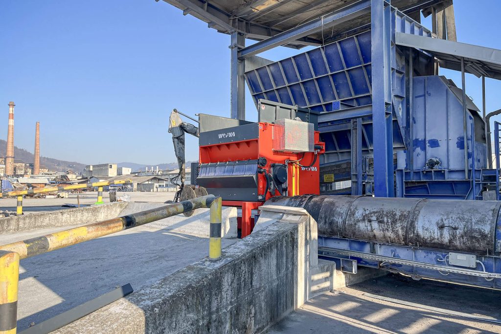 Orange shredder on an industrial site in front of a large blue machine