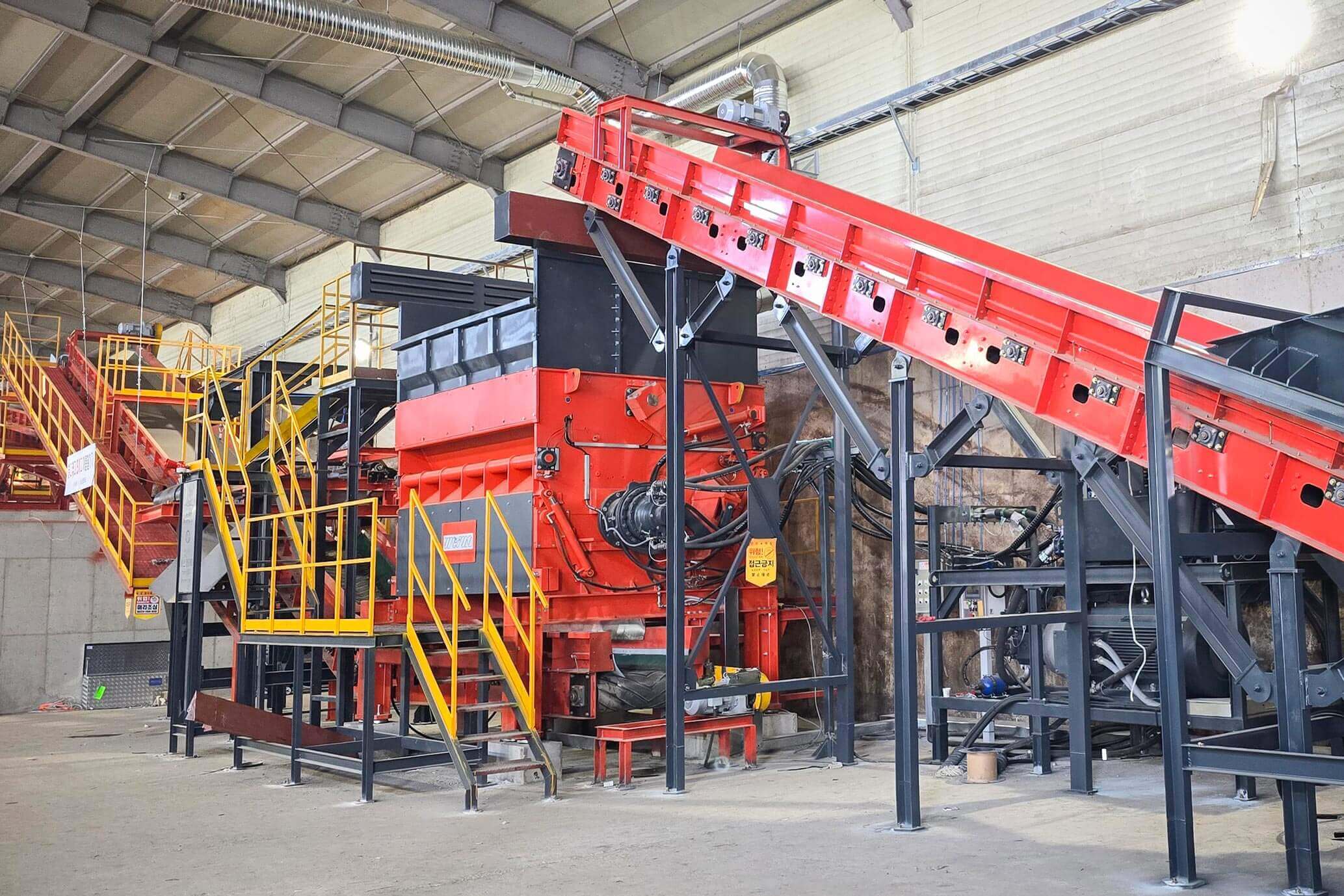 An orange shredder in a warehouse built into a recycling line with conveyor belts