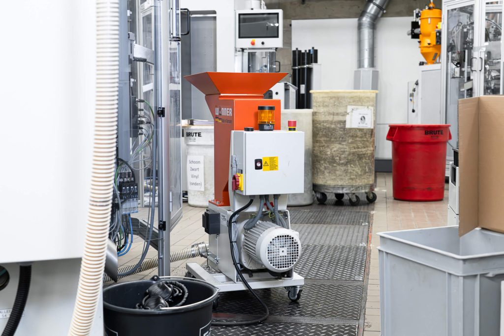 Rear view of a Wanner C-Series granulator next to a pressing machine for record production