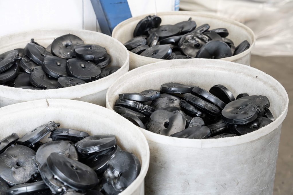 Discarded black PVC pucks for recycling, collected in white plastic container