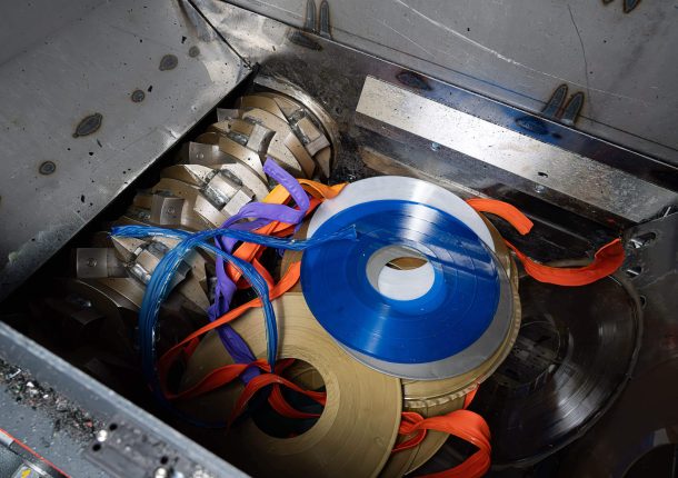 Colorful records lie in the cutting chamber of a shredder in front of the rotor with cutting blades