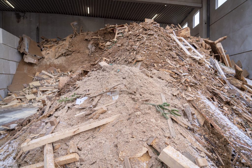 Large pile of wood scraps, boards, and branches in a warehouse at the Trier firewood factory.