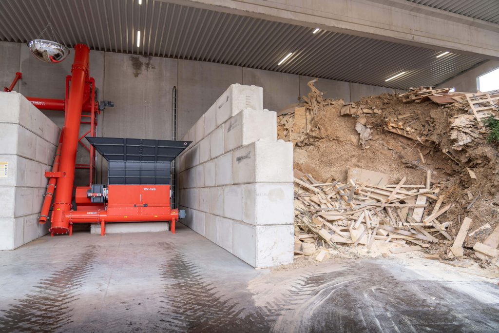 WEIMA WLK 2000 shredder next to a large pile of residual wood and sawdust in a hall of the Trier firewood factory.