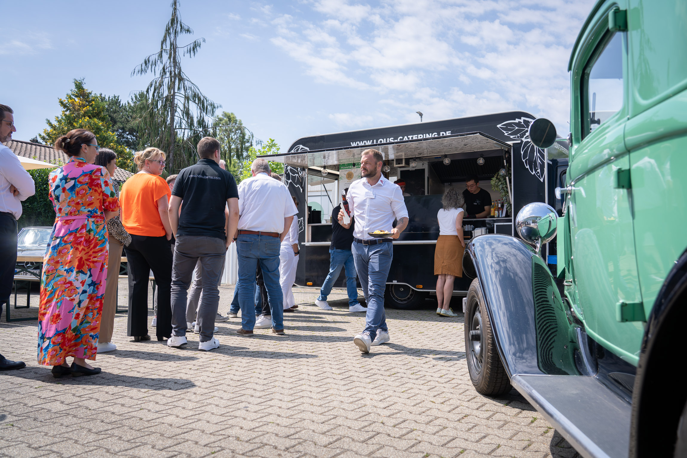 People queue for food in front of a food truck in bright sunshine