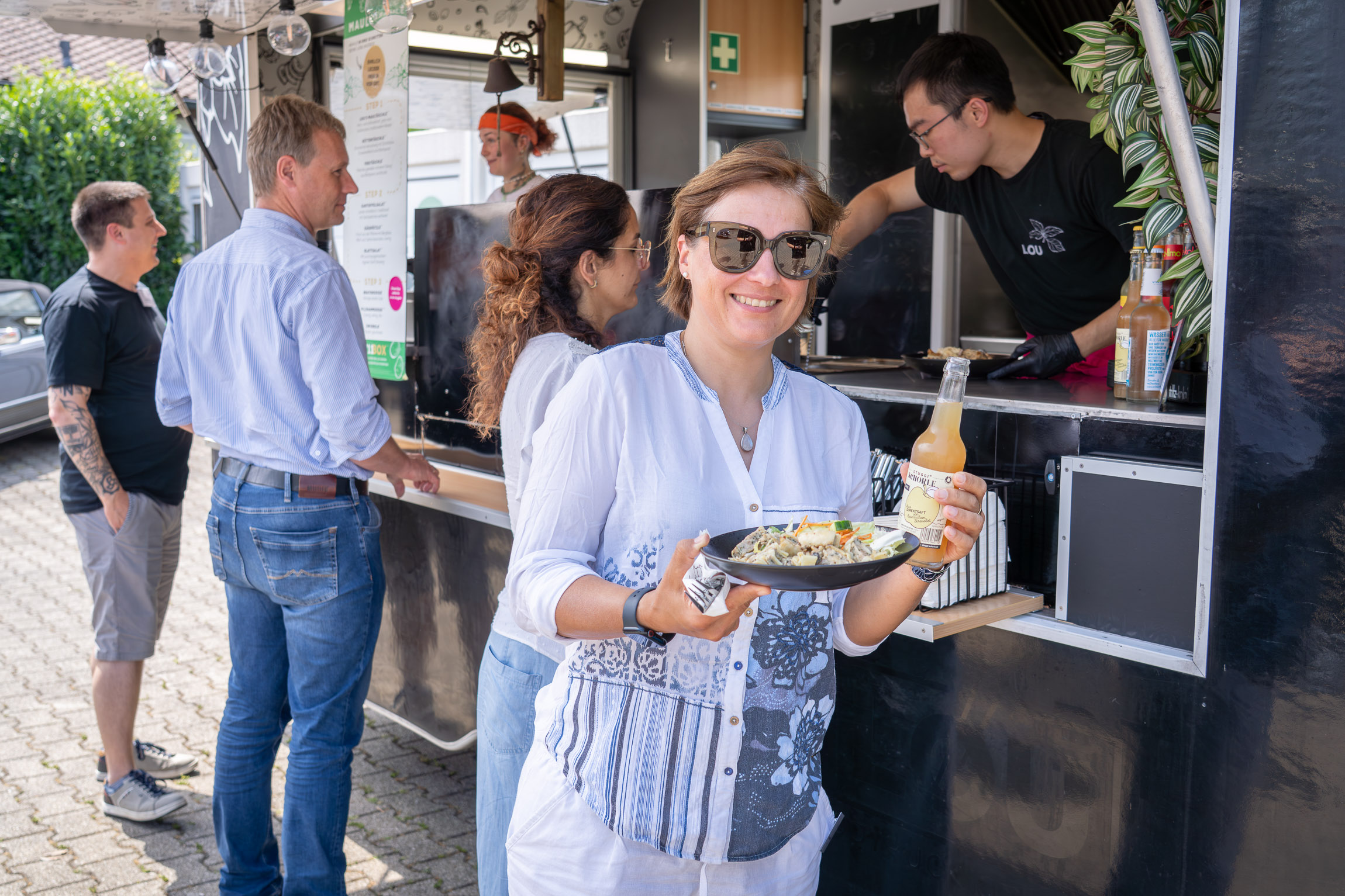 A woman stands in front of a food truck and grins into the camera with her plate of Maultaschen