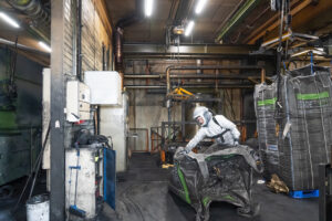 A man in a white protective suit holding an empty black big bag in the hall of a tire manufacturer.