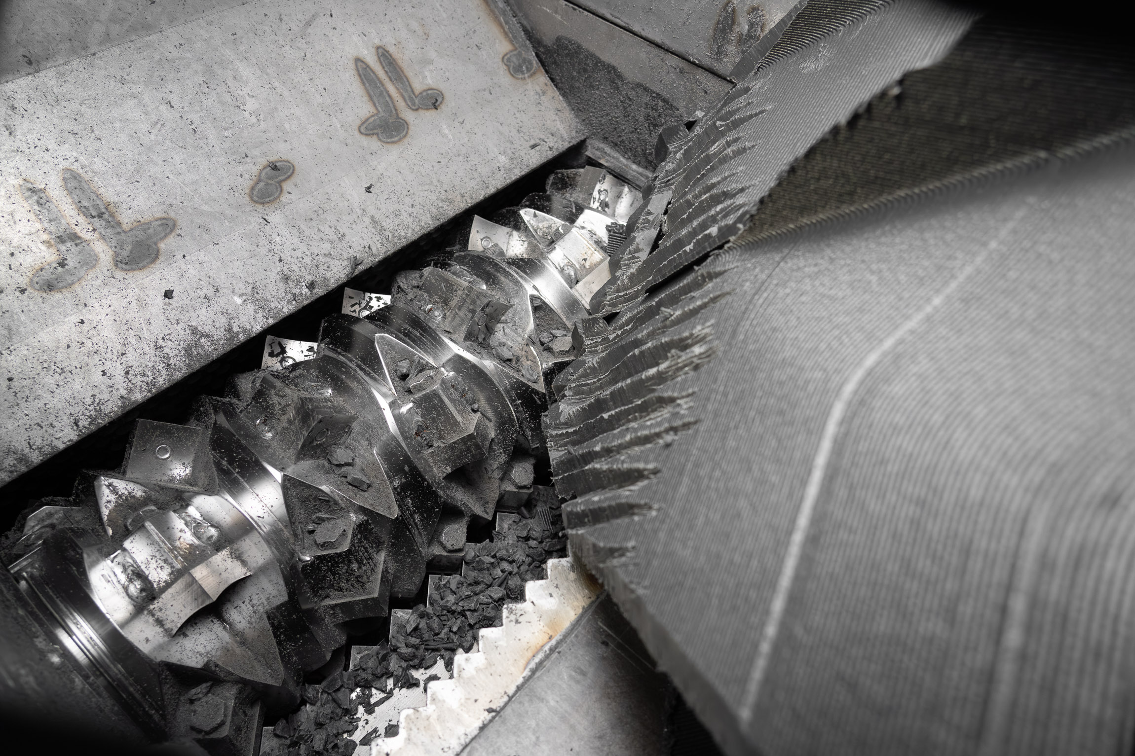 Inside a shredder with a shiny rotor shredding a big piece of black plastic