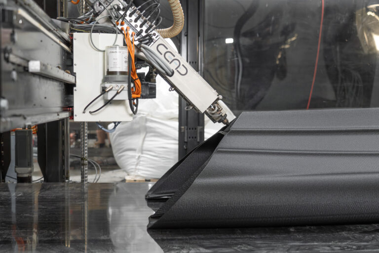 A large format 3D printer prints a black boat
