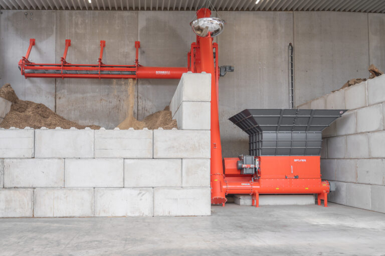 A WEIMA shredder with a screw conveyor is located in a covered hall, which transports the shredded material to a bunker.