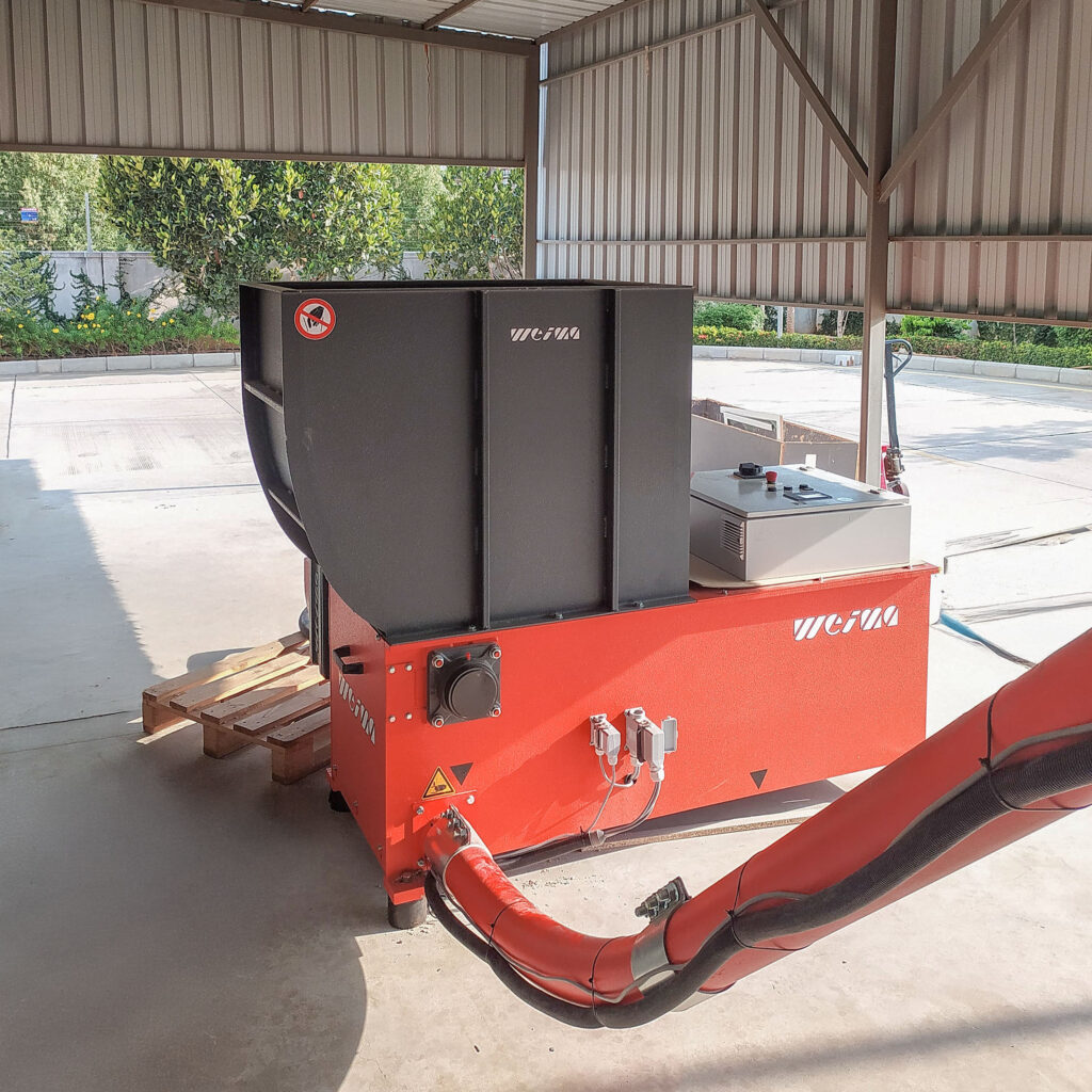 A small orange shredder for wood shredding with a connected conveyor channel for wood chips.