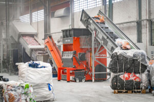 The WEIMA machine in a hall, with a conveyor belt and industrial plastic waste in front of it