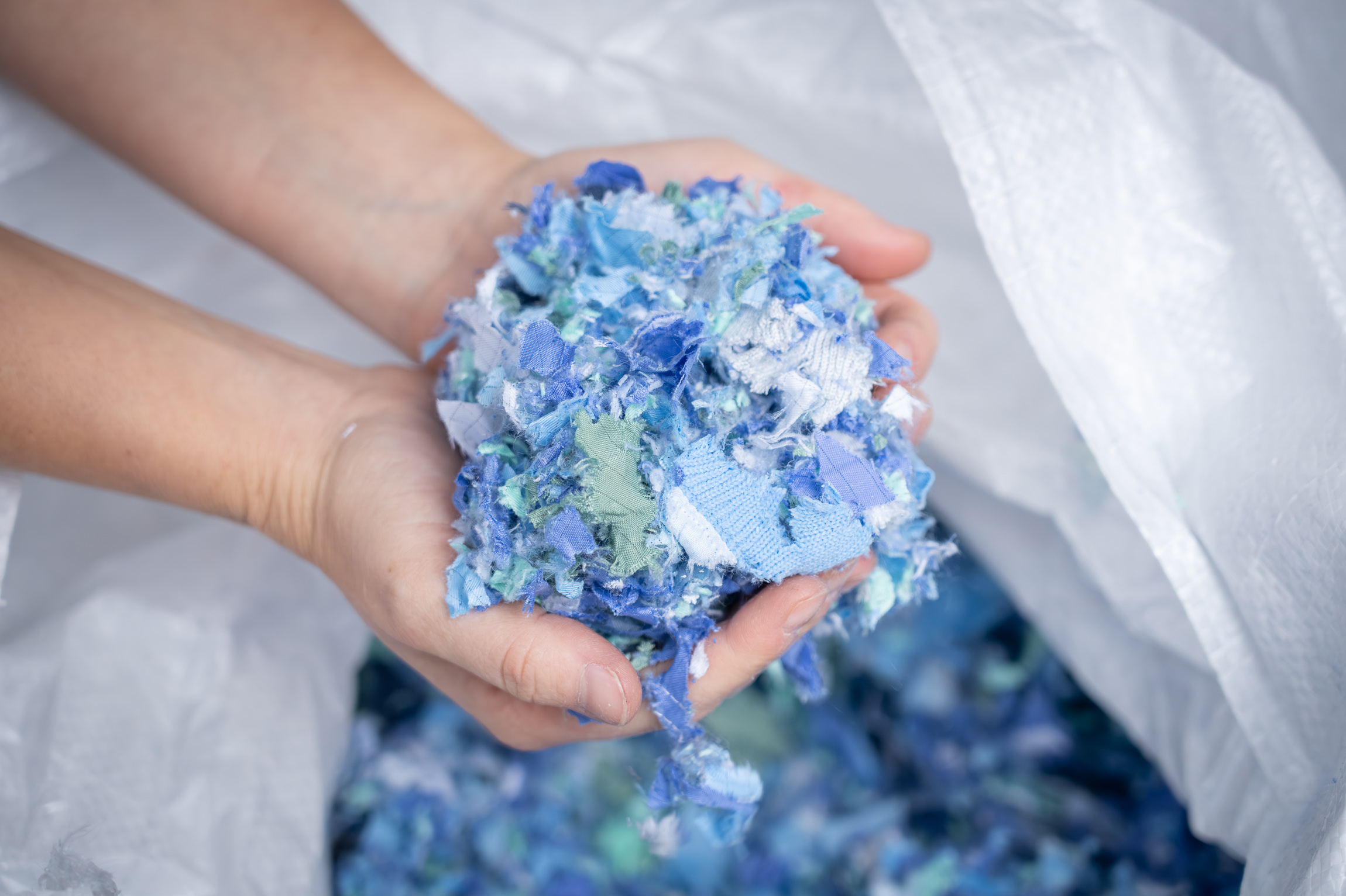 Shredded textiles held in both hands over a big bag