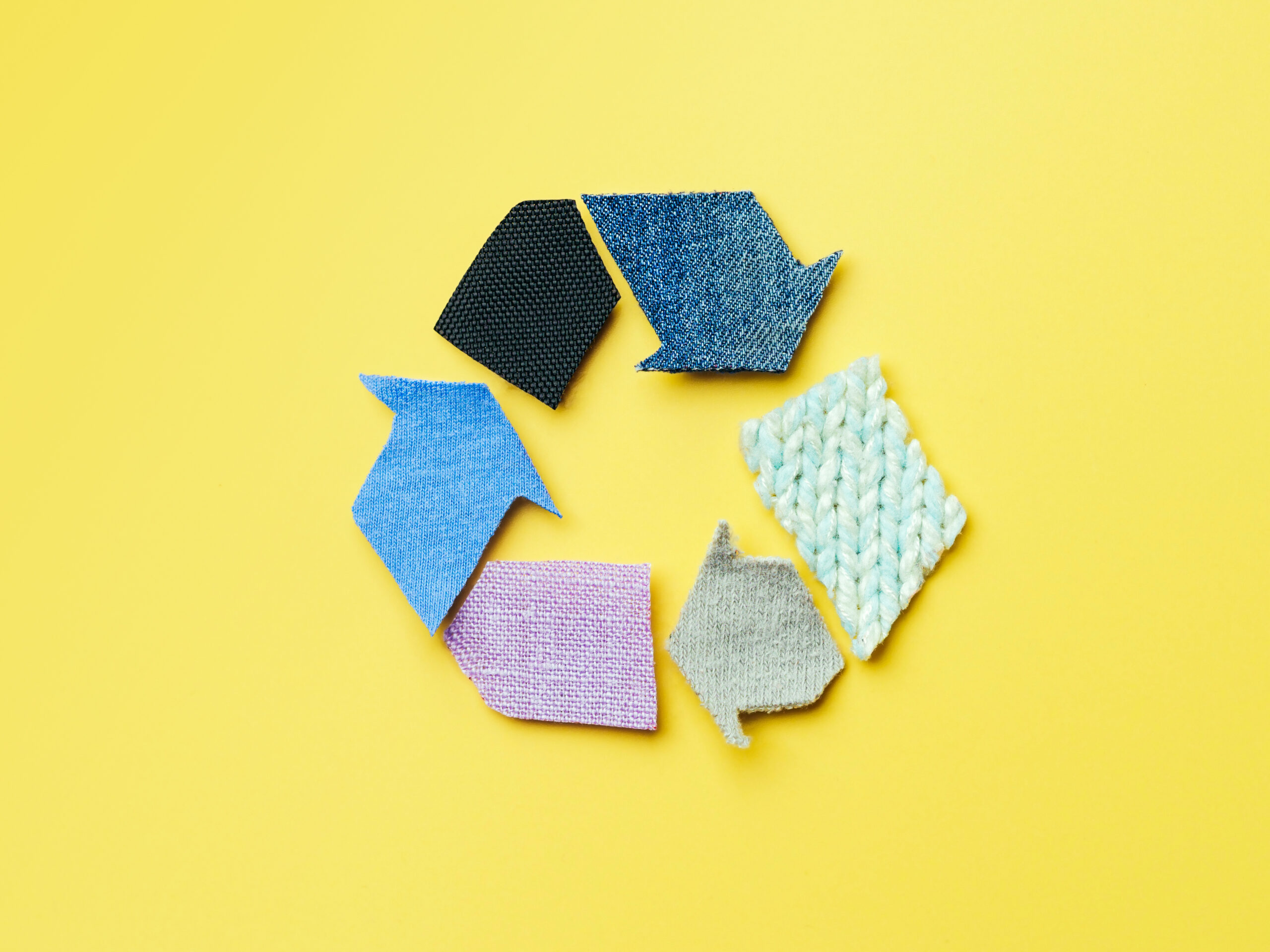 Reuse, reduce, recycle concept background. Recycle symbol made from old clothing on yellow background. Top view or flat lay.