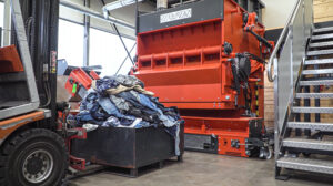 A box full of jeans in front of an orange WEIMA shredder